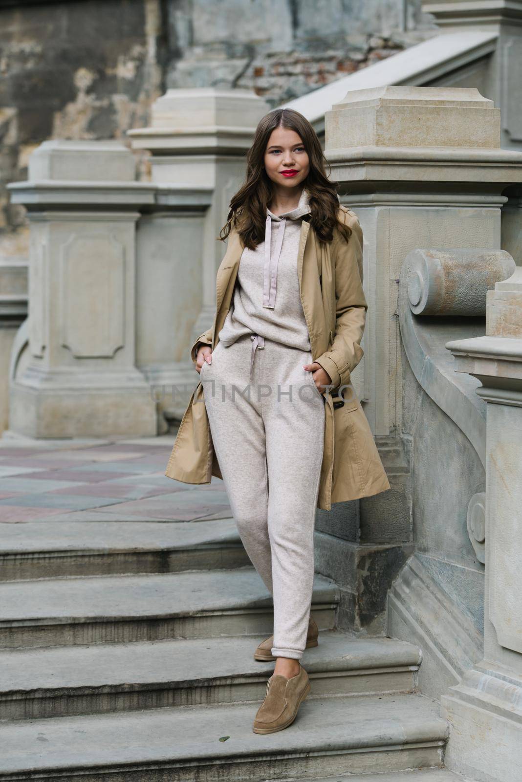 Portrait of fashionable women in beige sports suit, trench coat and stylish suede loafer posing on the stone stairs by Ashtray25