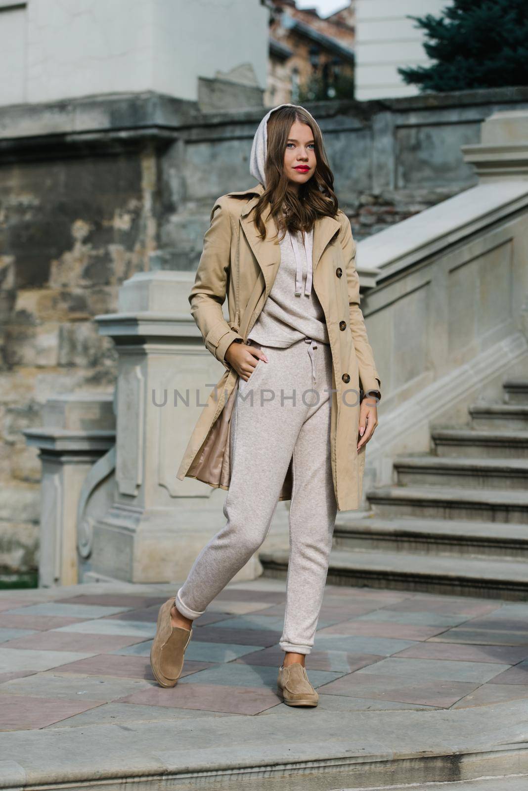 Portrait of fashionable women in beige sports suit, trench coat and stylish suede loafer posing on the stone stairs by Ashtray25