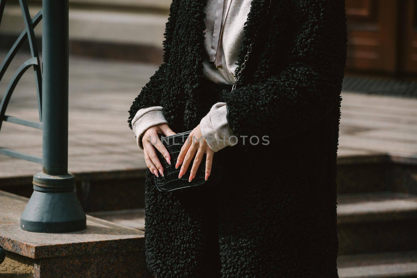 Fashion photo of young woman in black fur coat, jeanse and shoes at city street. beige jacket with a hood