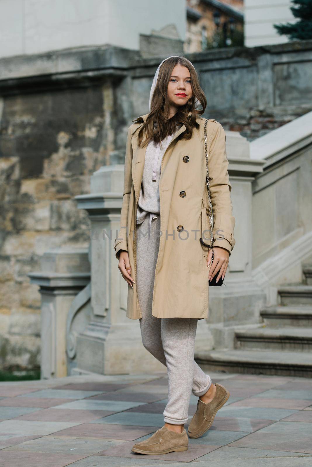 Portrait of fashionable women in beige sports suit, trench coat and stylish suede loafer posing on the stone stairs by Ashtray25