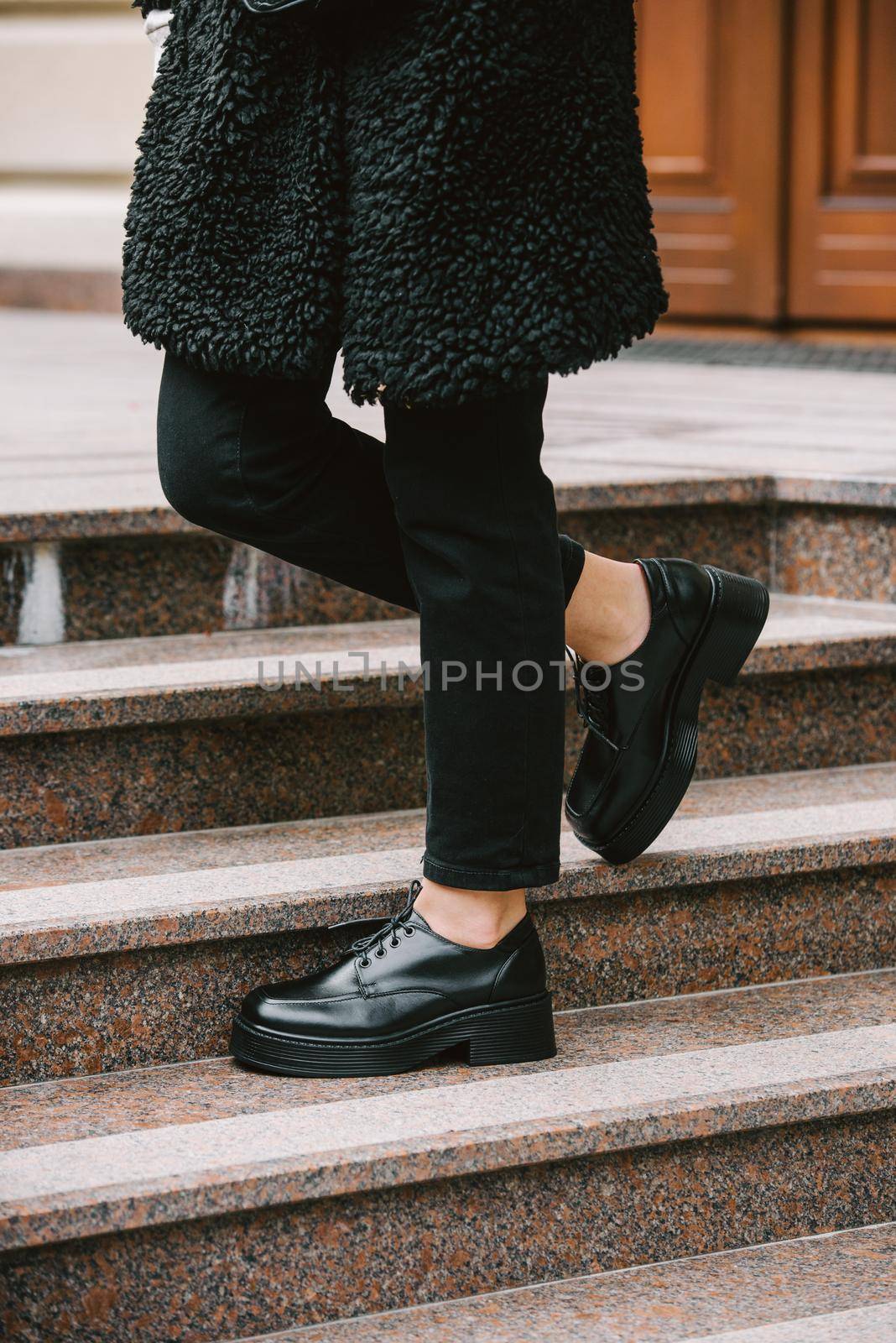 Fashion photo of young woman in black fur coat, jeanse and shoes at city street