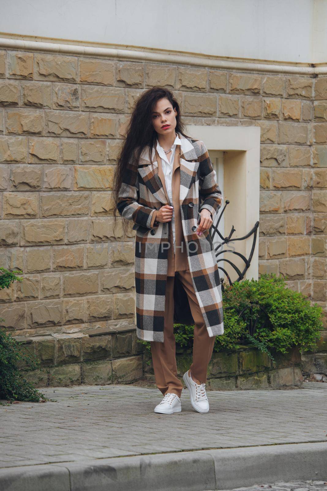 Closeup portrait of young beautiful fashionable woman wearing checkered long coat, beige pants and white blouse . Lady posing on city street. by Ashtray25