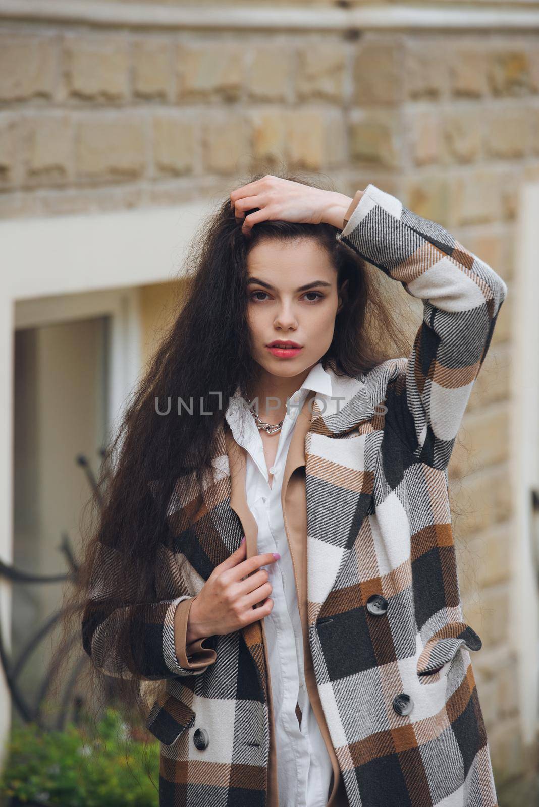 Closeup portrait of young beautiful fashionable woman wearing checkered long coat, beige pants and white blouse . Lady posing on city street. by Ashtray25