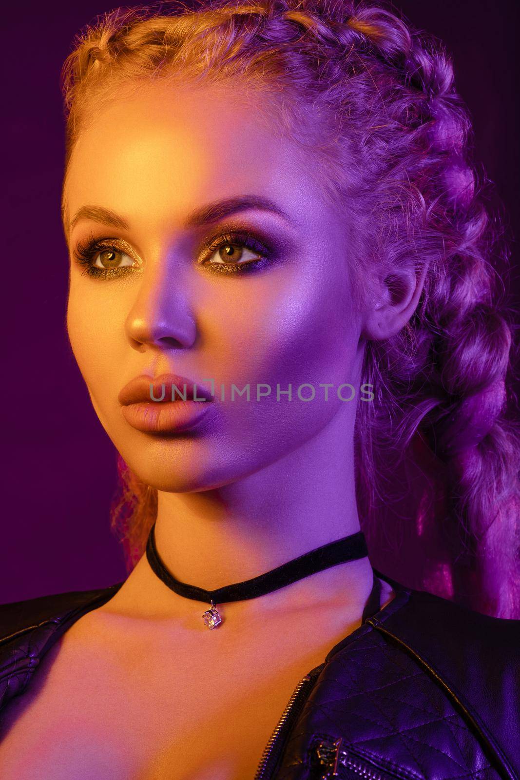 Fashion portrait of stunning sexy young blonde woman with trendy braids and sparkling bra under the net top. She is holding peace sign by the eye, making pouting lips in bright pink and yellow light.