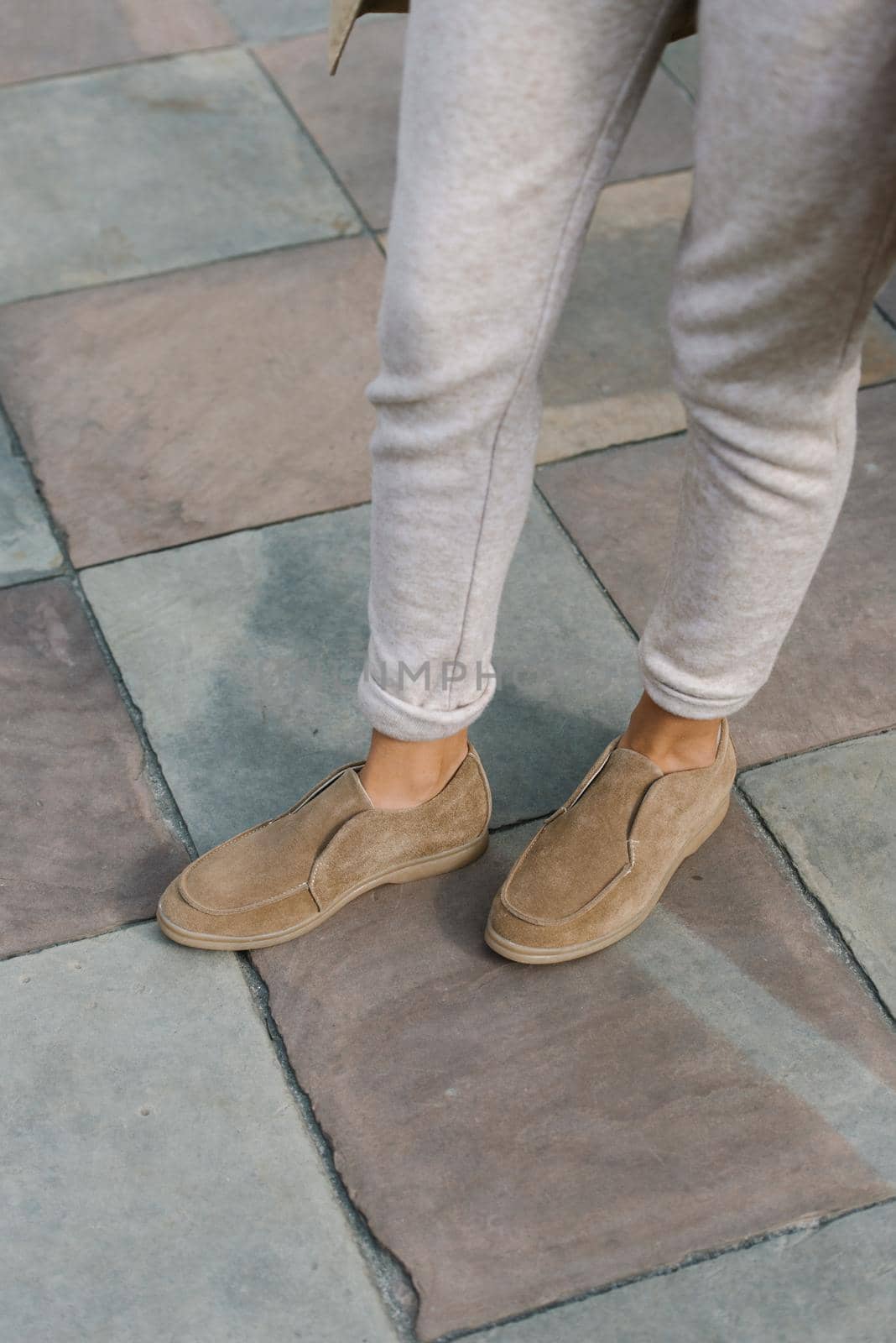 Portrait of fashionable women in beige pants and stylish suede loafer shoes posing in the street. Stone tiles