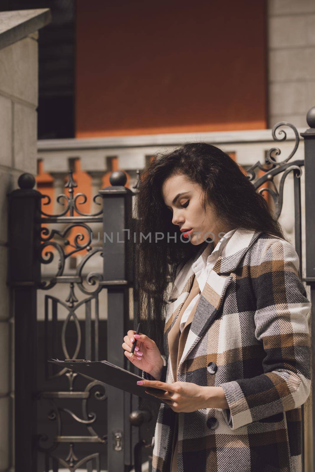 Female real estate agent with clipboard outdoors. woman wearing a white blouse and a checkered coat