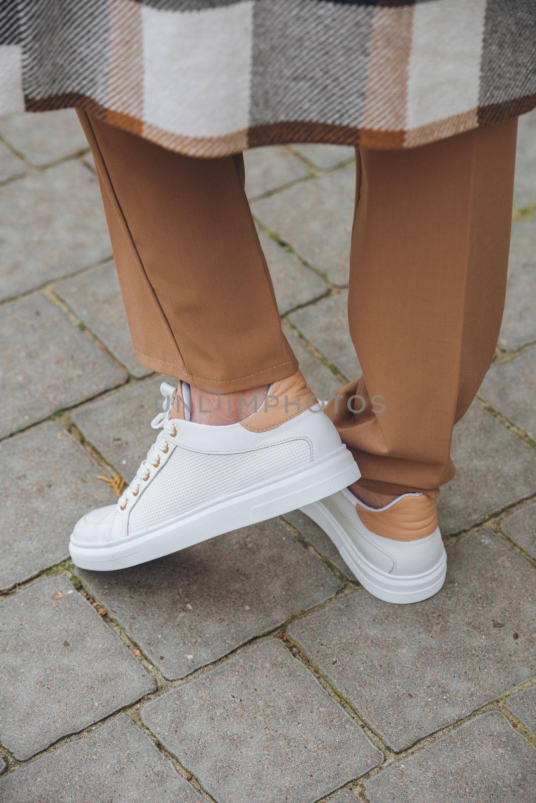 Closeup photo of beautiful fashionable woman wearing checkered long coat, beige pants, white blouse and sneakers. by Ashtray25