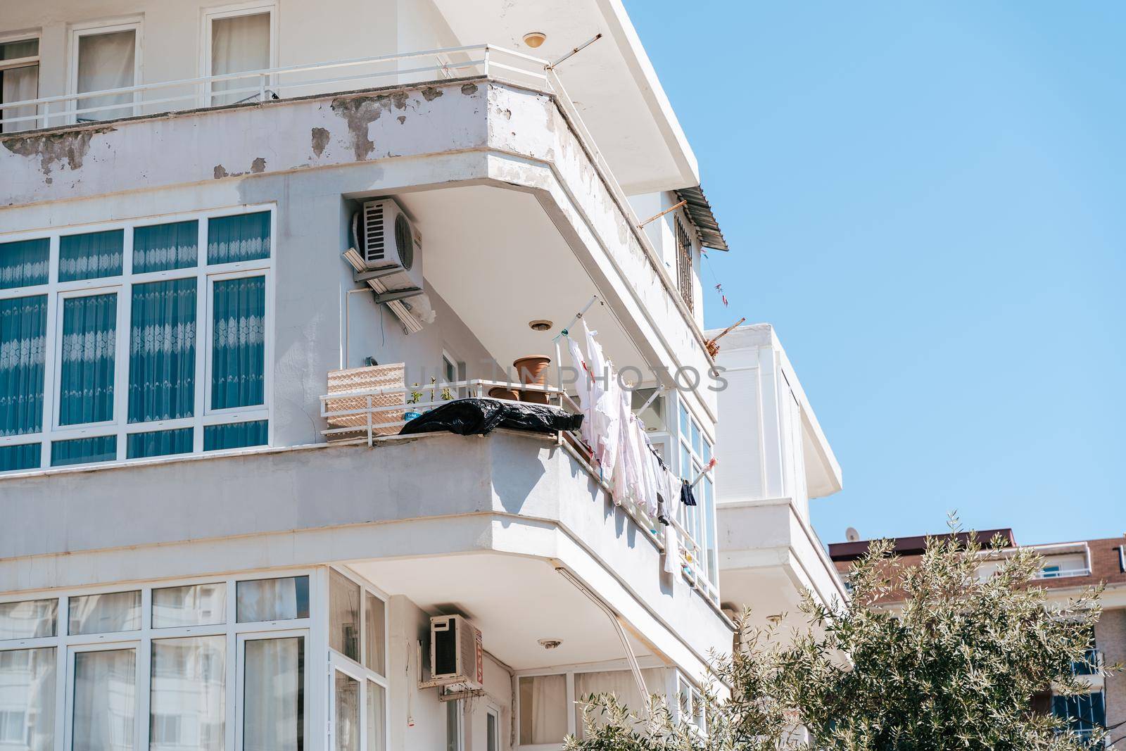 White shabby rundown residential building with drying clothes on the balcony. Simple people living. Scuffed worn-out residential block with old air conditioning system.