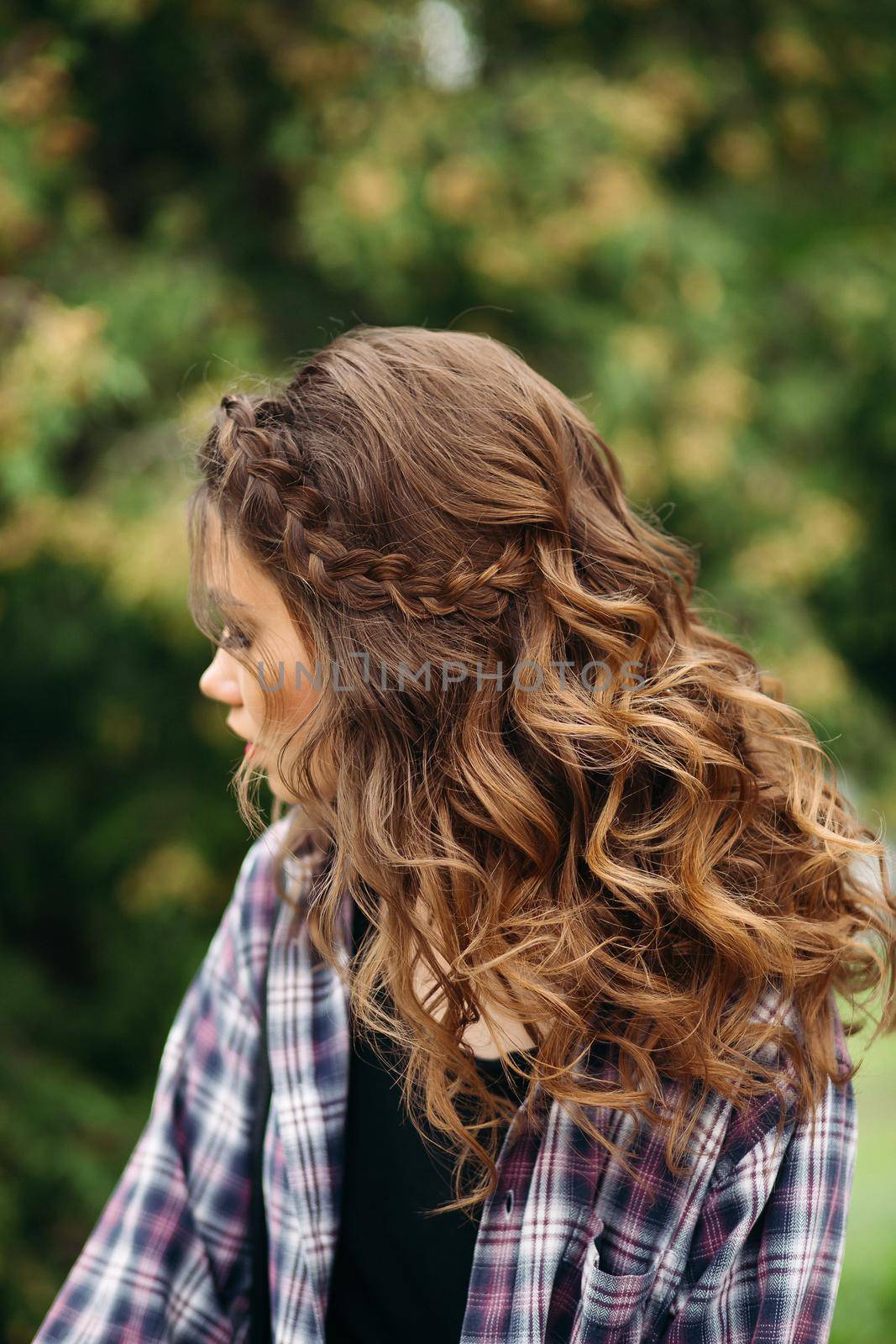 Portrait of incognito woman with volumed curly hairstyle after beauty salon, looking away. Gorgeous hipster girl wearing in cheeked shirt, walking at street. Fashion and style.