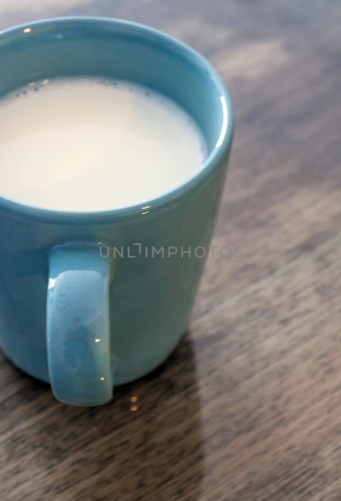 Milk in a blue cup on the wooden and top glass table