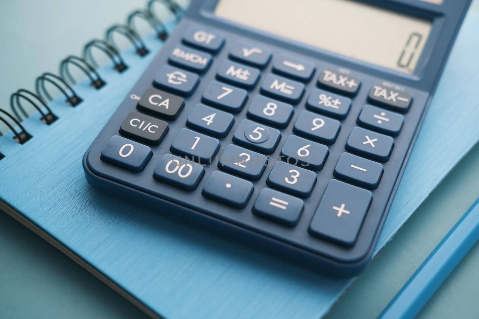 Close up of blue calculator and notepad on color background .