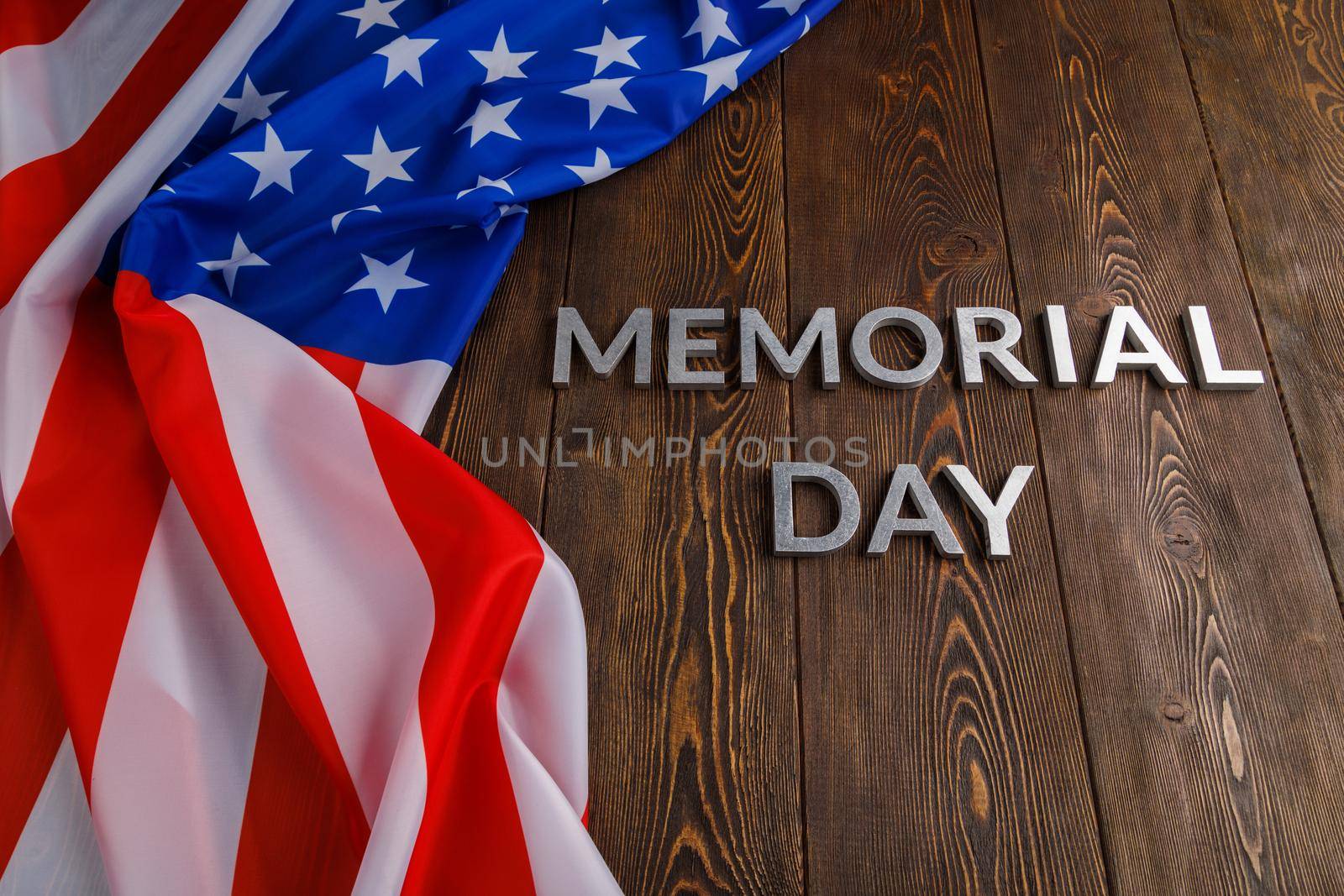 the words memorial day laid with silver metal letters on wooden board surface with crumpled usa flag.
