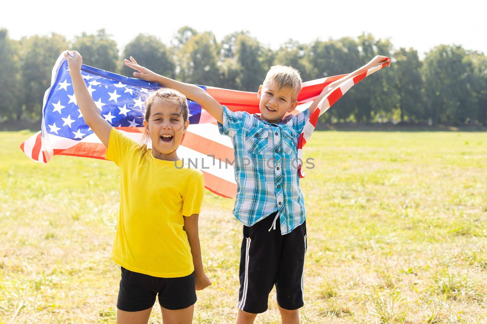 Happy Caucasian girl and boy smiling laughing holding hands and waving American flag outside celebrating 4th july, Independence Day, Flag Day concept