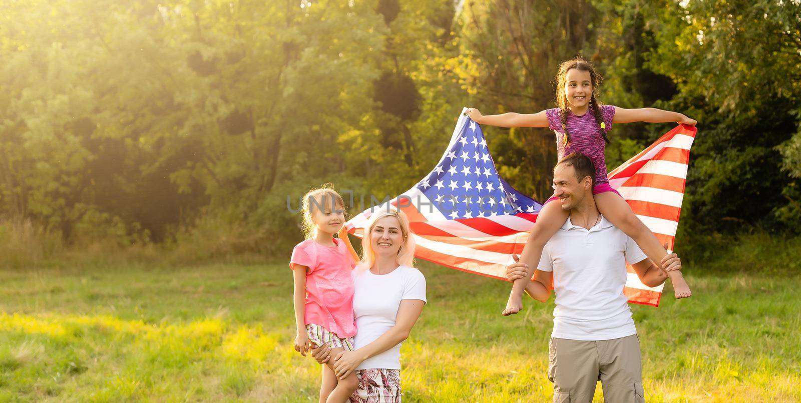 Patriotic holiday. Happy family, mother and daughters with American flag outdoors on sunset. USA celebrate independence day 4th of July. by Andelov13