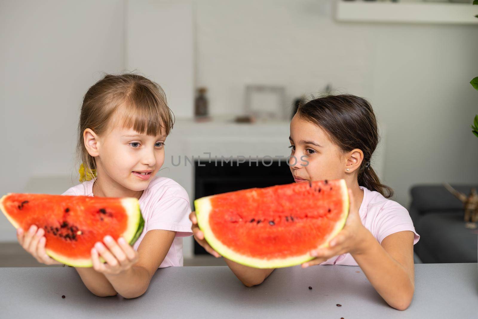 Funny little sisters eating fresh juicy watermelon at home.