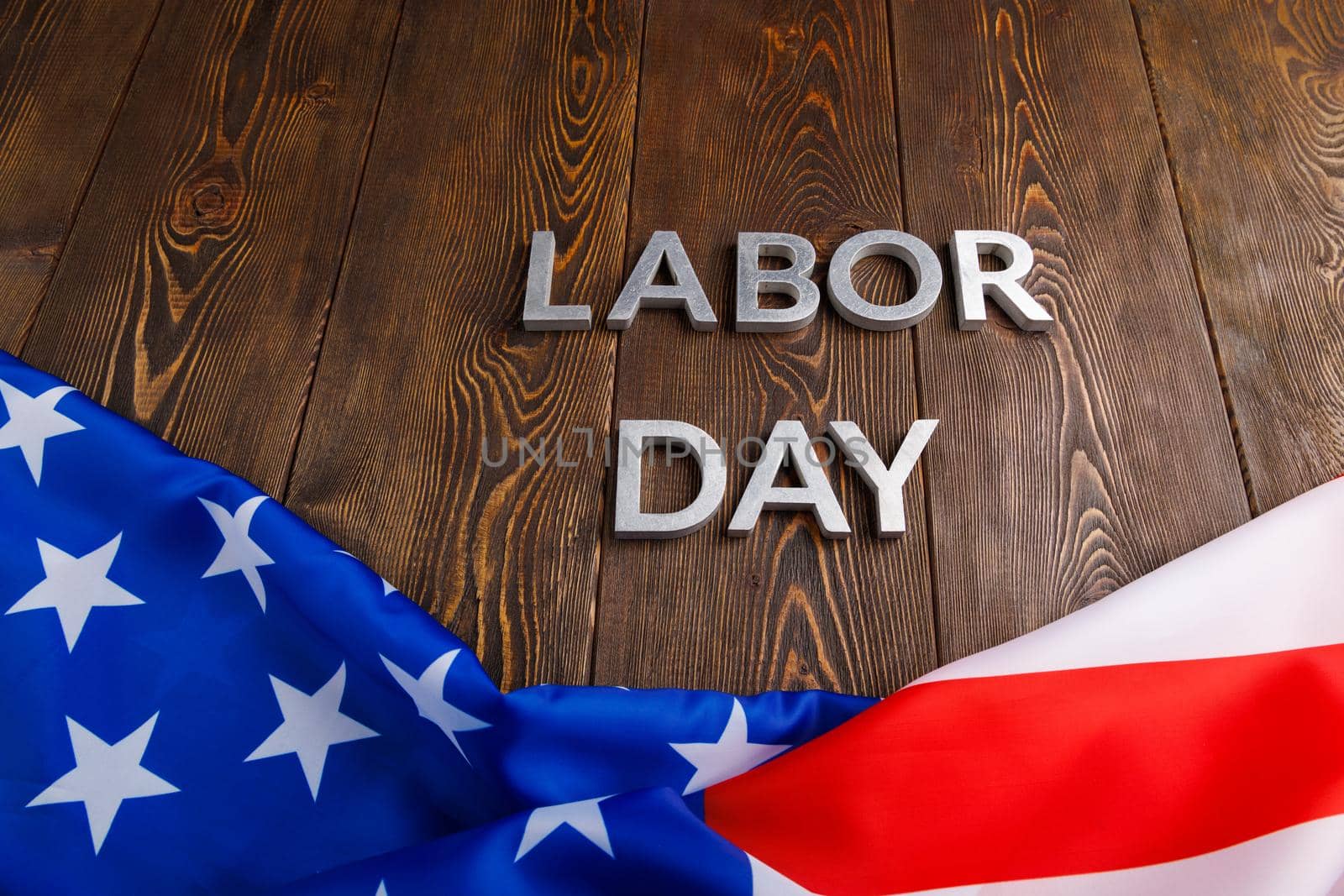 words labor day laid with silver metal letters on wooden surface with crumpled USA flag on bottom side in linear perspective view