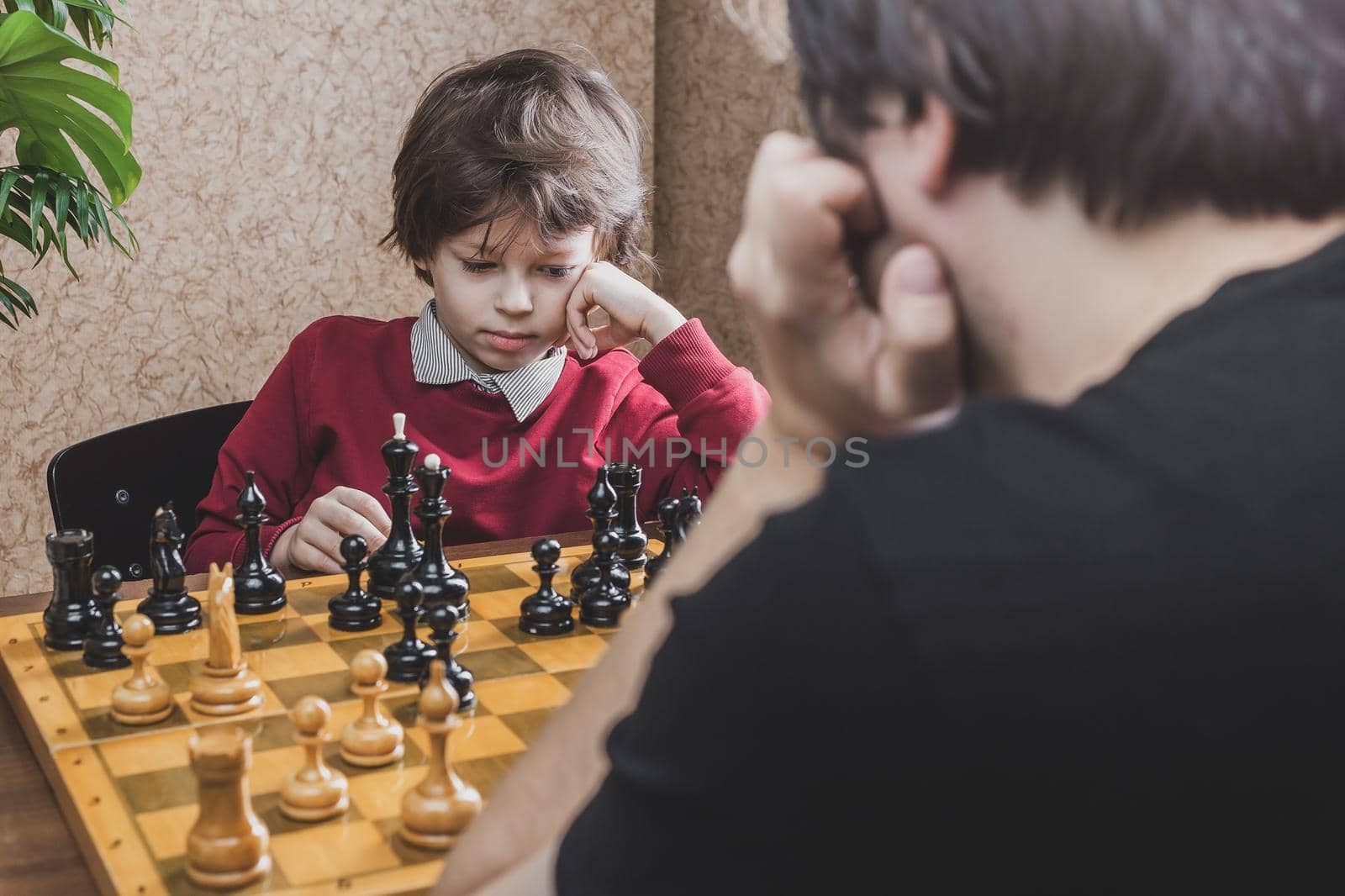 Thoughtful six years old boy playing chess with his father pondering on making move. Leisure activities during quarantine