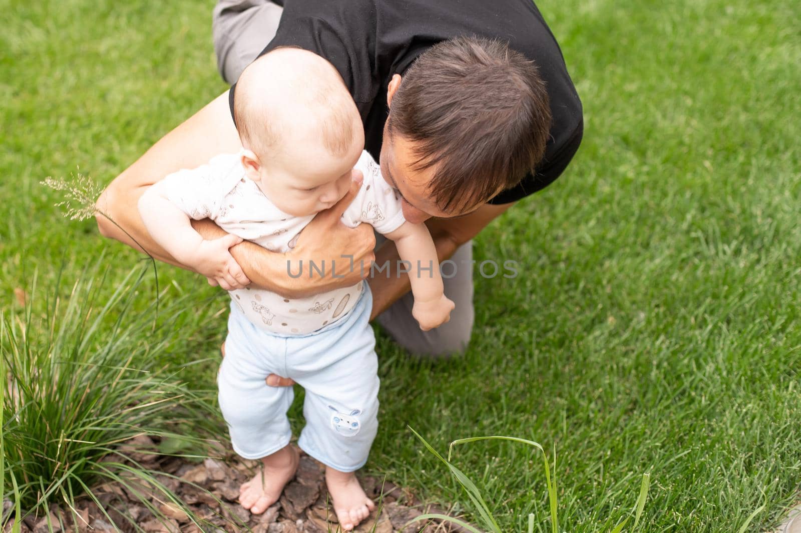 baby boy taking first steps with father help in a park by Andelov13