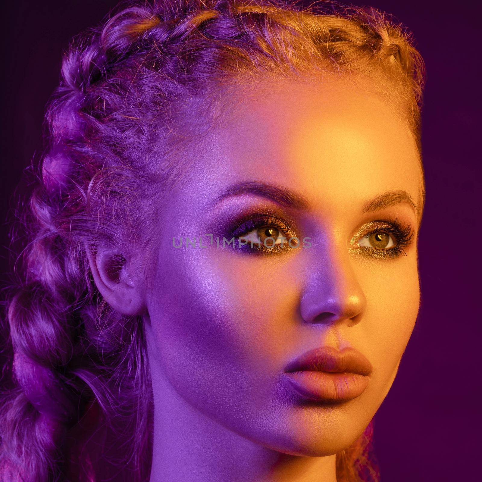 Fashion portrait of stunning sexy young blonde woman with trendy braids and sparkling bra under the net top. She is holding peace sign by the eye, making pouting lips in bright pink and yellow light.