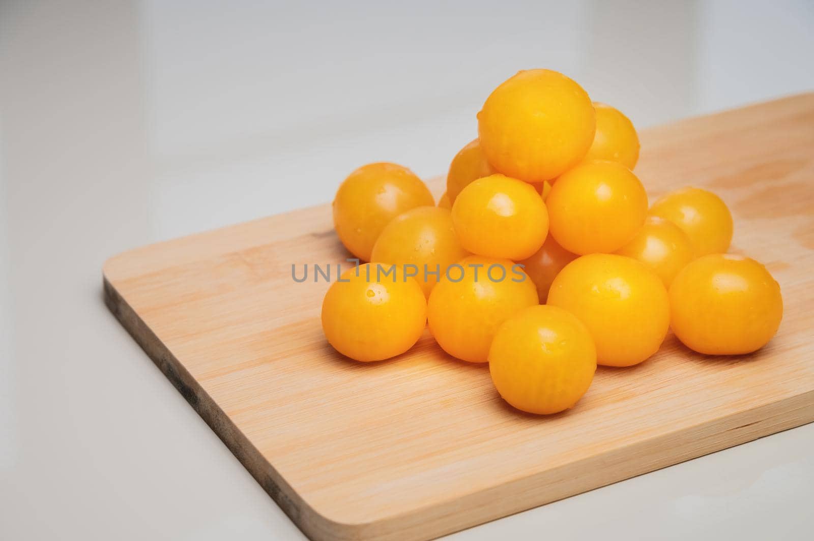 A heap of yellow cherry tomatoes on a wooden cutting board in the kitchen on a white table.