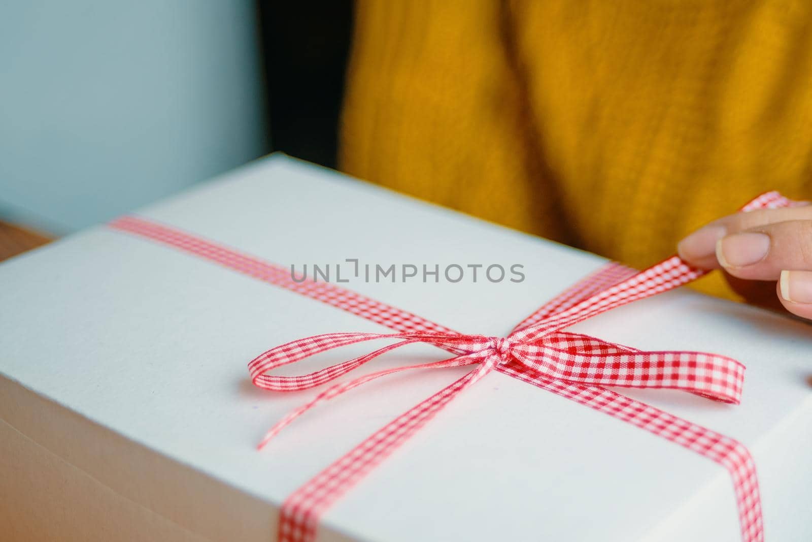 Girl's fingers hold red checkered ribbon on gift box. Holiday mood. Festive surprise for Christmas, New Year or Birthday.