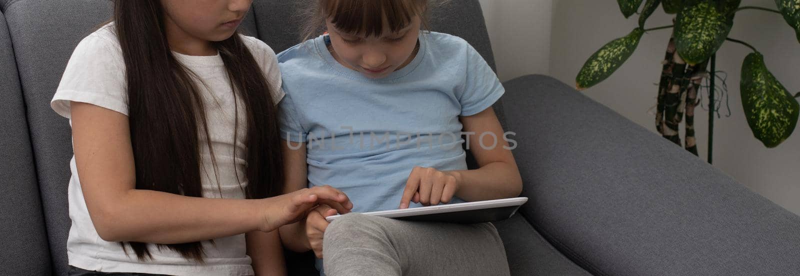 Closeup portrait of two smiling girls lying on couch and using tablet.