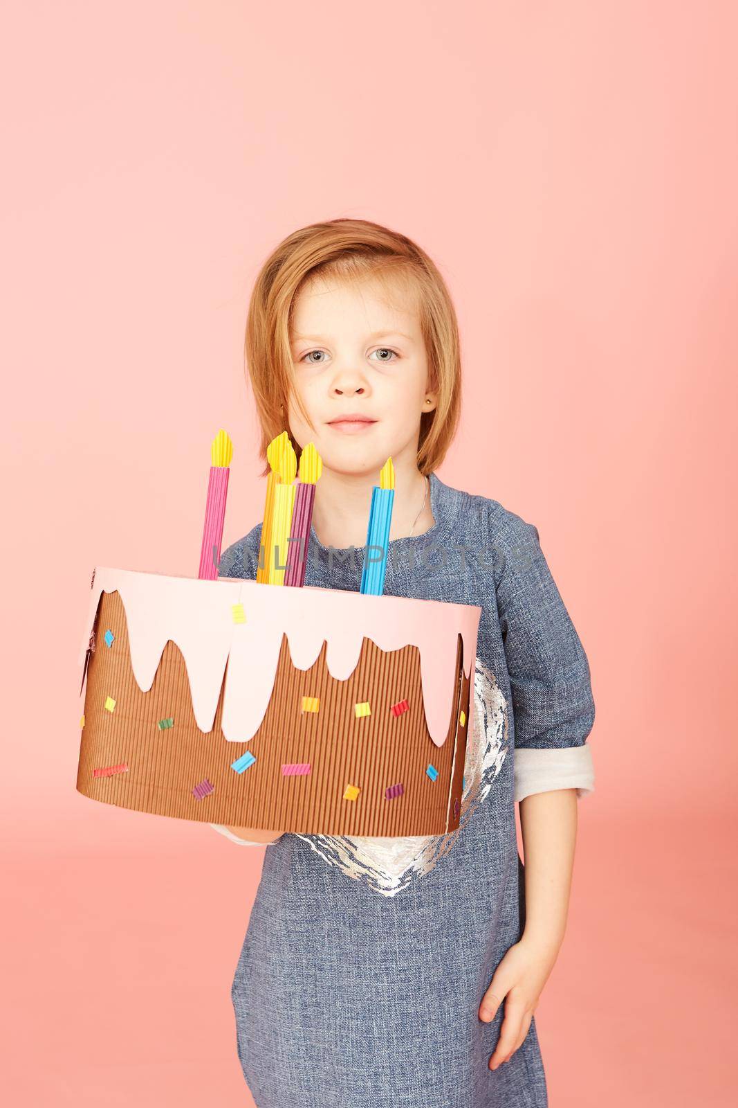 Portrait of an excited pretty little girl celebrating birthday and showing cake on over pink background