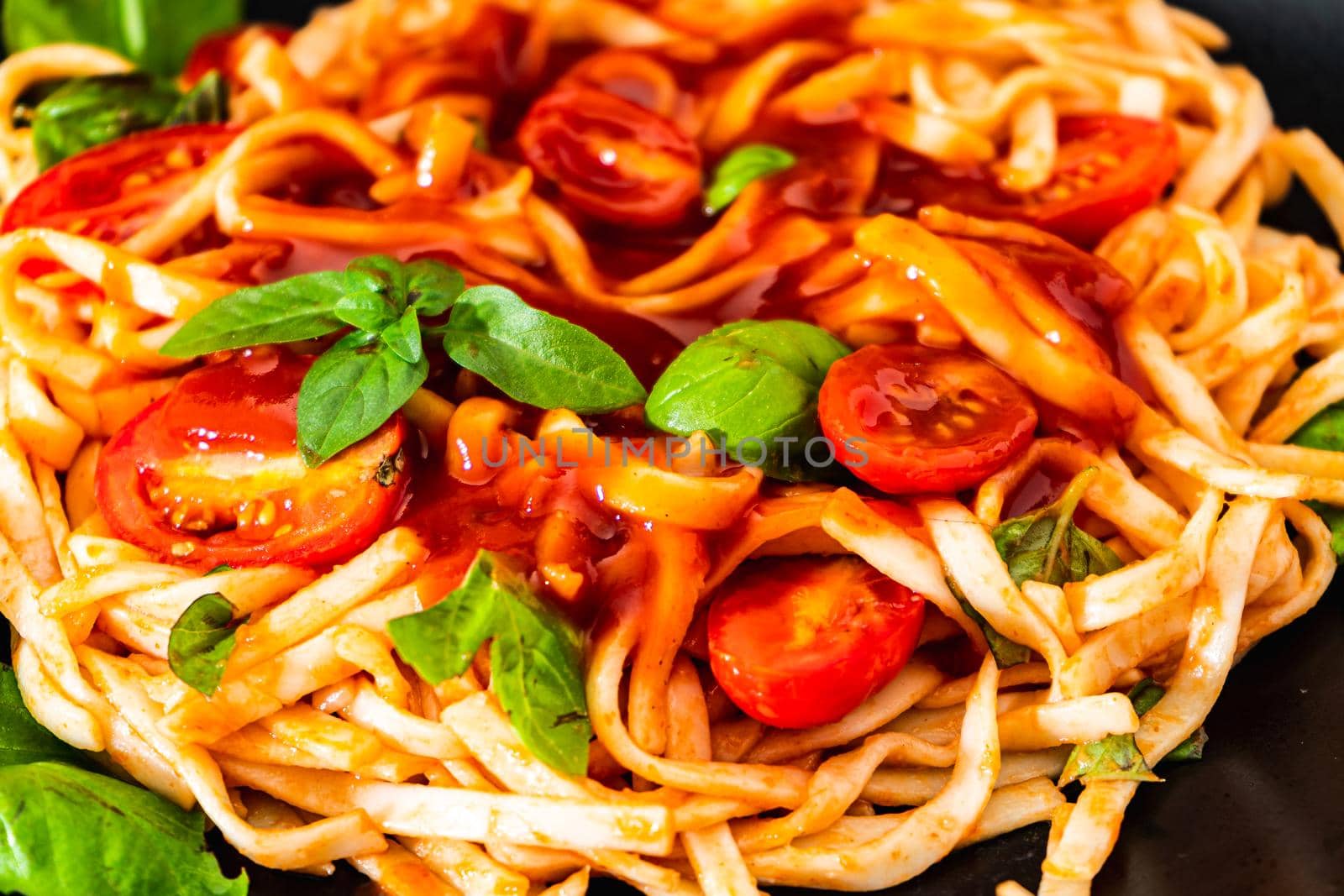 Spaghetti pasta with an exquisite homemade tomato sauce with homemade basil leaves served on a black plate on a rustic table. Close up. High view.