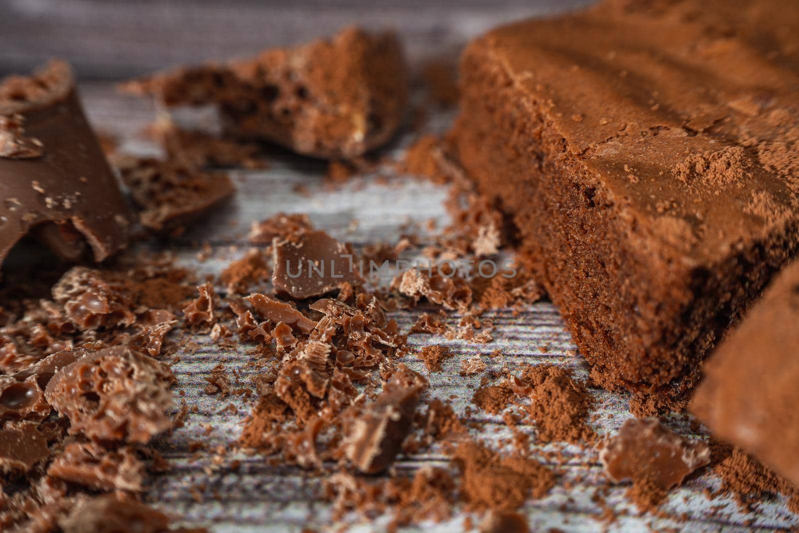 Close up of a Chocolate brownies on a rustic wooden table with chocolate chips and chocolate soil next to the brownie portions.