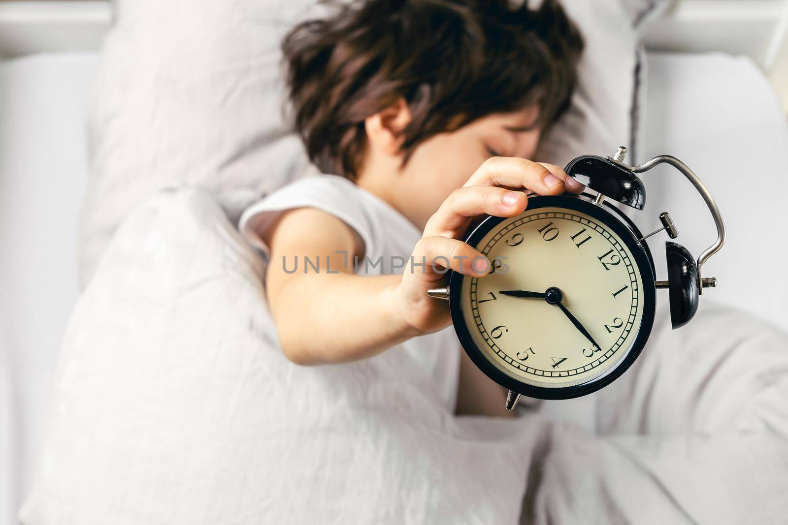 Boy holding alarm clock showing quarter past seven by Syvanych