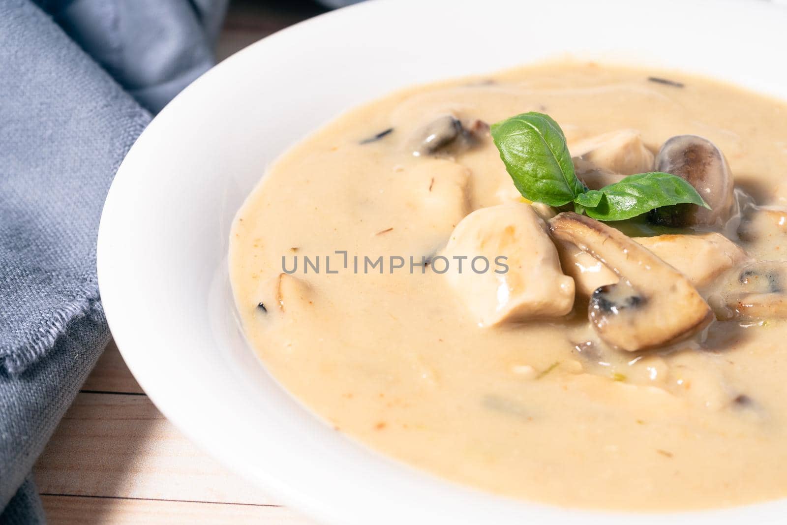 A Homemade cream of chicken and mushroom soup or French style chicken fricassee, in a white soup bowl on a wooden table. High view. Close-up