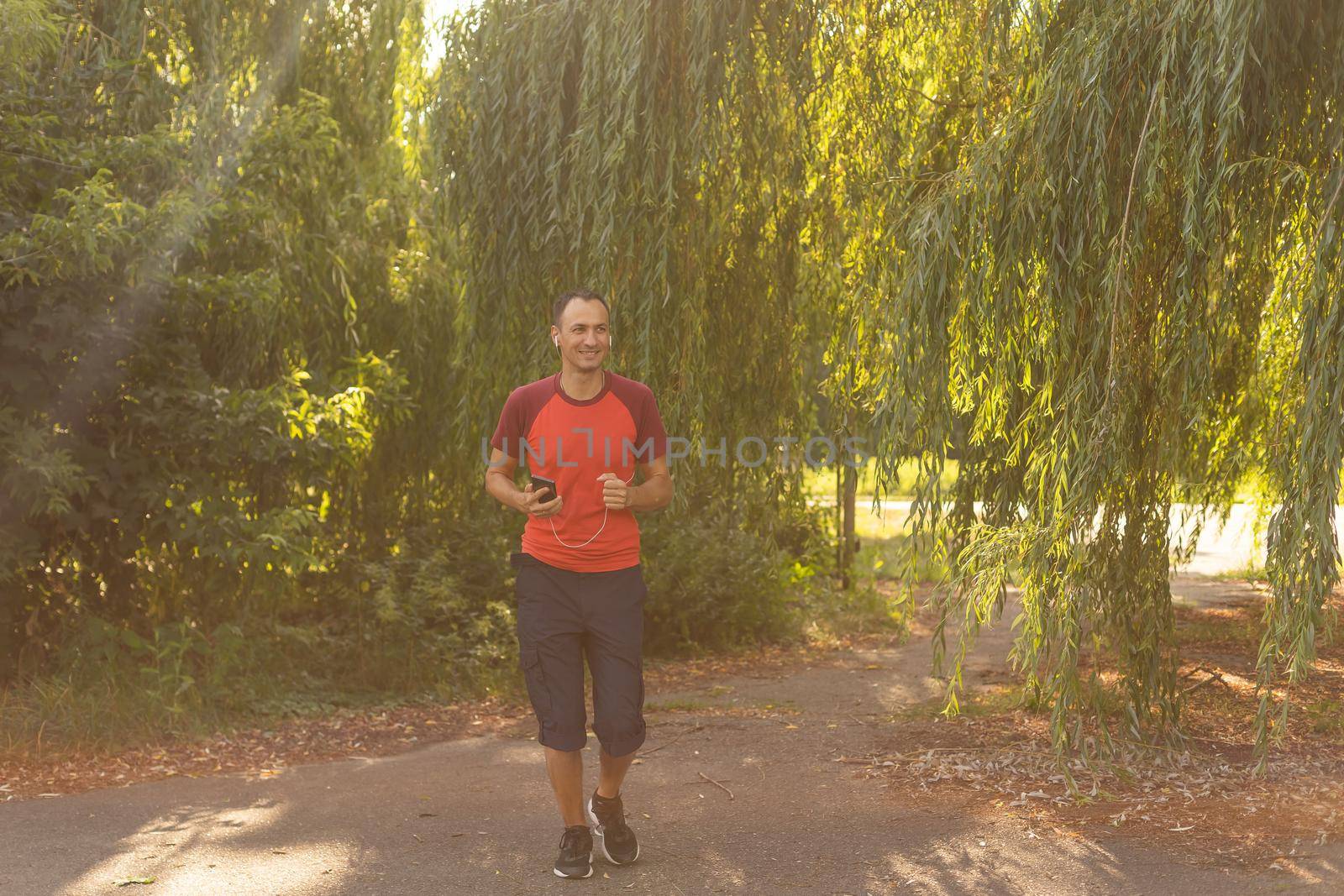 Portrait of a man running in a park. Close up of a smiling man running while listening to music using earphones.