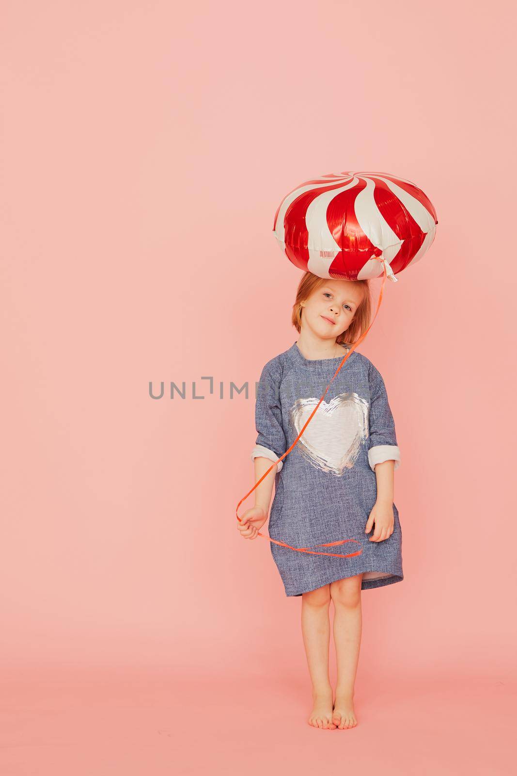 Portrait of an excited pretty little girl celebrating birthday and holding balloon in hand on over pink background. by sarymsakov