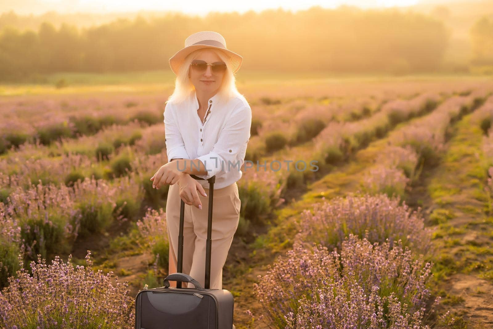 Beautiful young woman in lavender field standing with suitcase by Andelov13