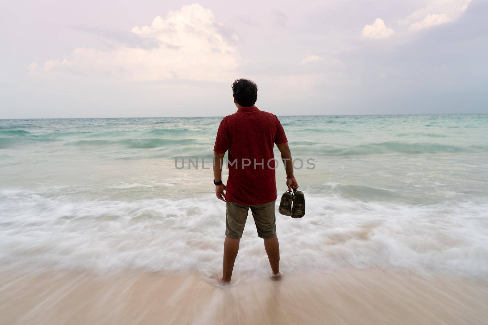 Long exposure shot of person holding up slippers dripping sea water with the corn blue water waves in the background showing beach life at havelock andaman islands in India by Shalinimathur