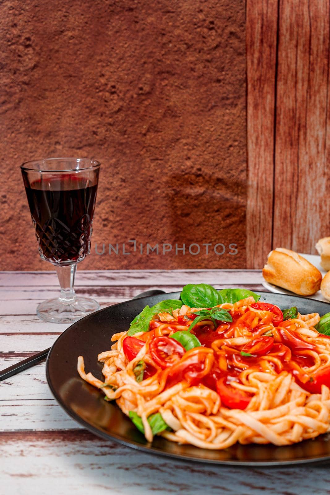 Spaghetti pasta with an exquisite homemade tomato sauce with homemade basil leaves served on a black plate with a glass of wine on a rustic table. Vertical orientation. Copy space.