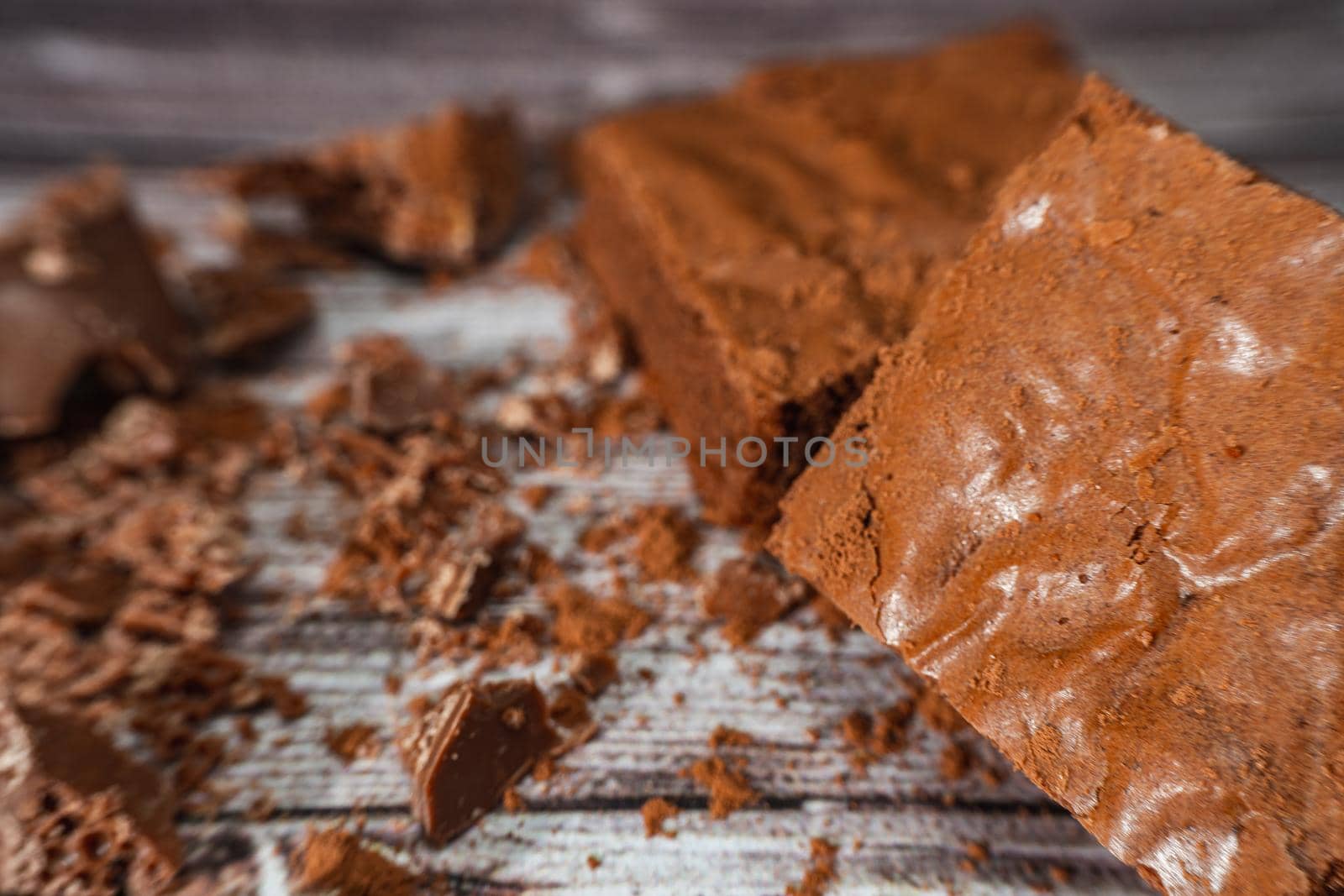 Close up of a Chocolate brownies on a rustic wooden table with chocolate chips and chocolate soil next to the brownie portions.