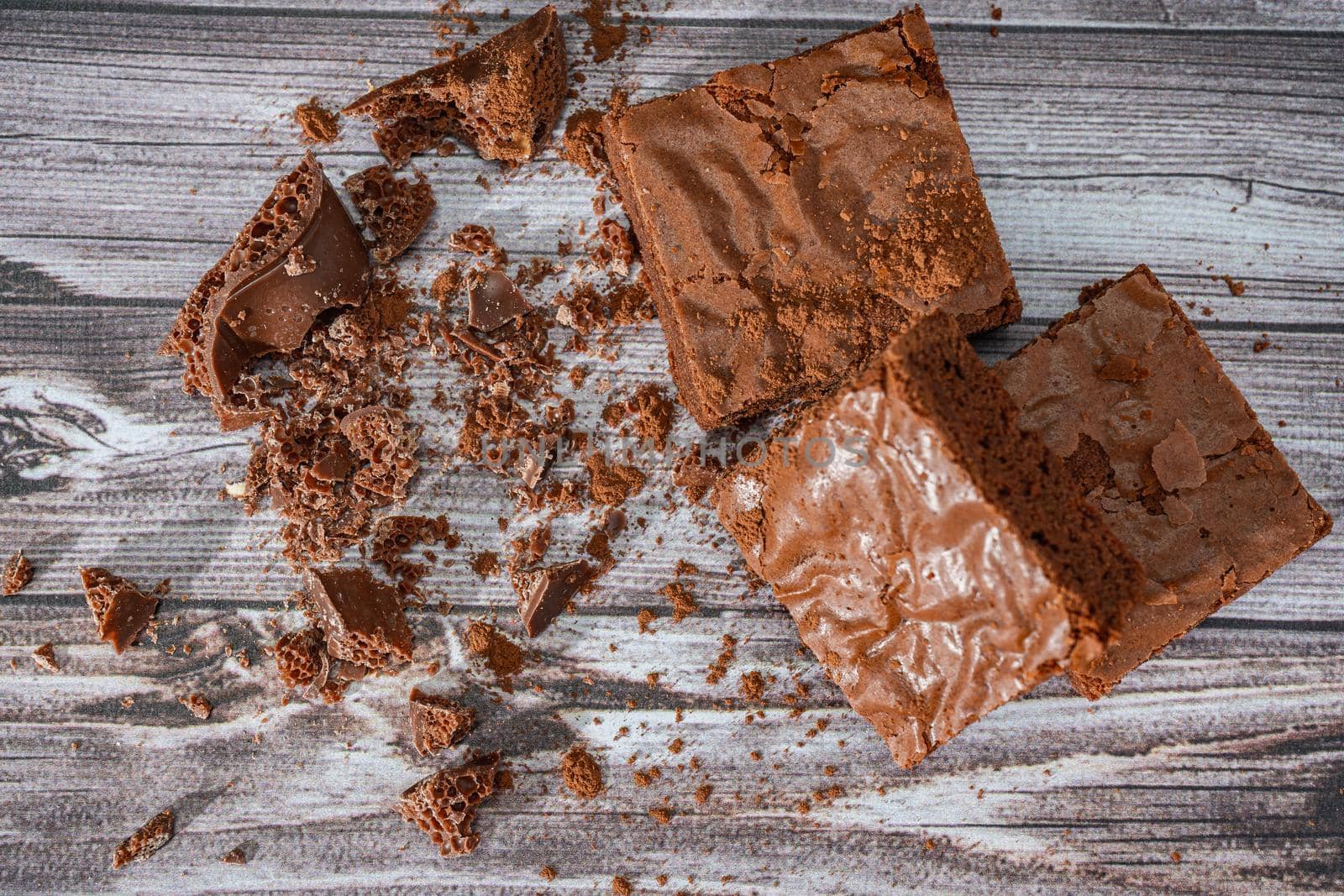 Chocolate brownies on a rustic wooden table with chocolate chips and chocolate soil next to the brownie portions.