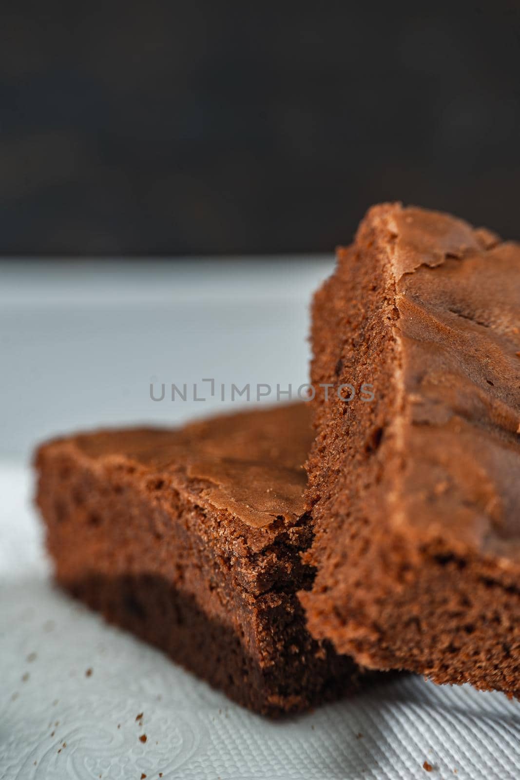 A cubes of chocolate brownies on a white plate on a marble table. Close up shot. vertical orientation.