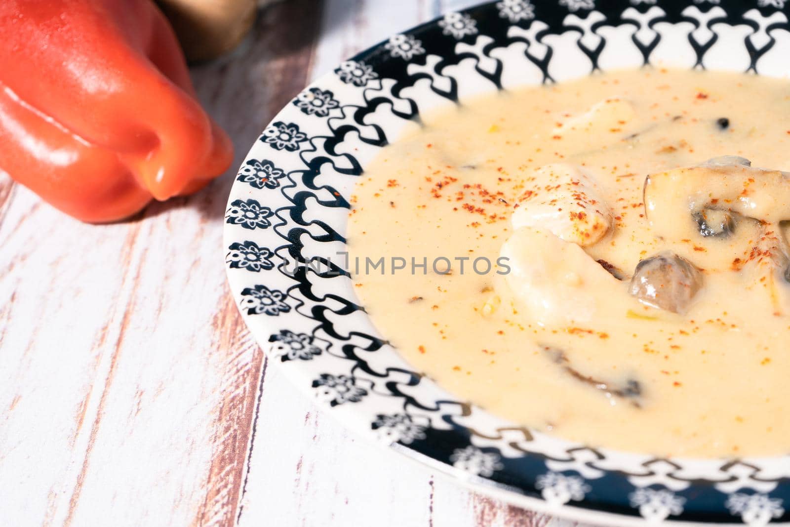 A Homemade cream of chicken and mushroom soup or French style chicken fricassee, in a soup bowl on a wooden table. High view. Close-up