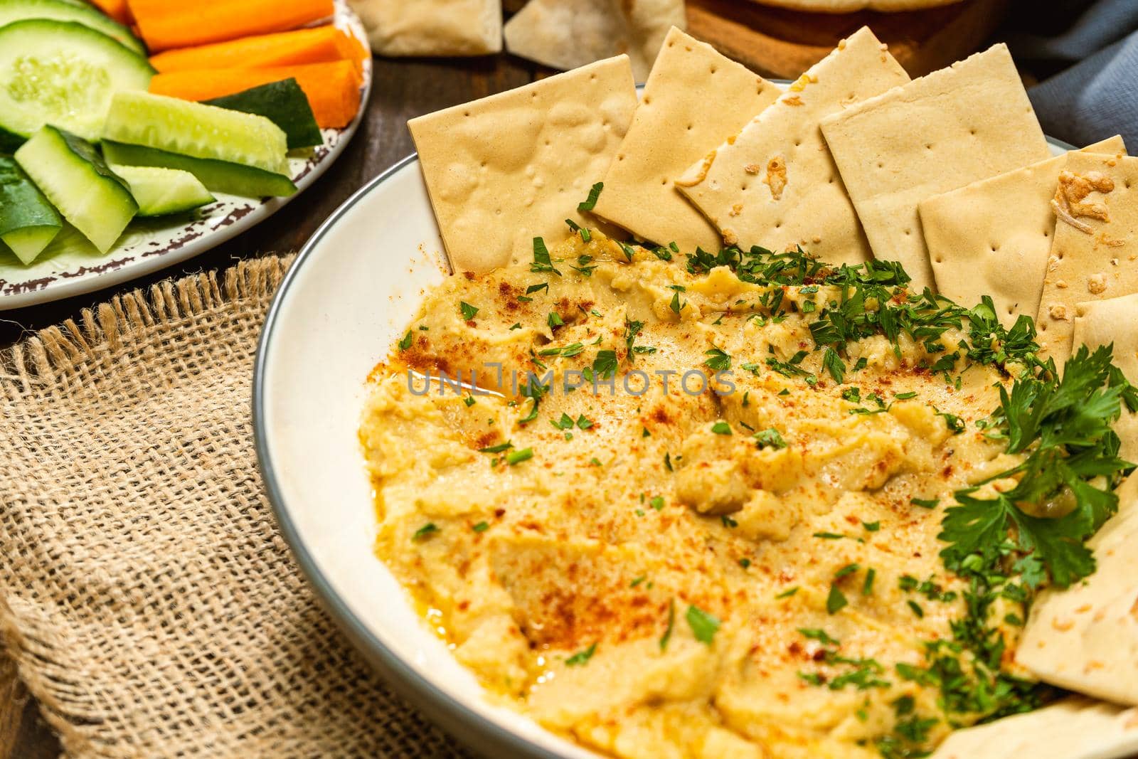 Close-up of a bowl with homemade Hummus with crackers and in another bowl carrots and other vegetables. Fresh, healthy and natural food concept.