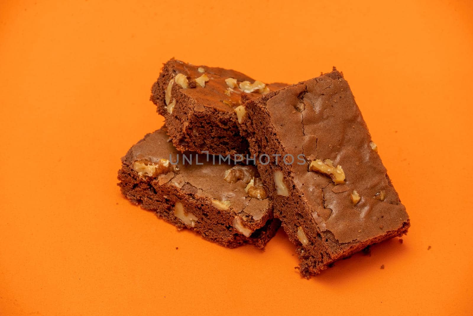 Homemade chocolate brownie squares with pecan pieces. Orange Background. Natural, healthy food concept. High view.