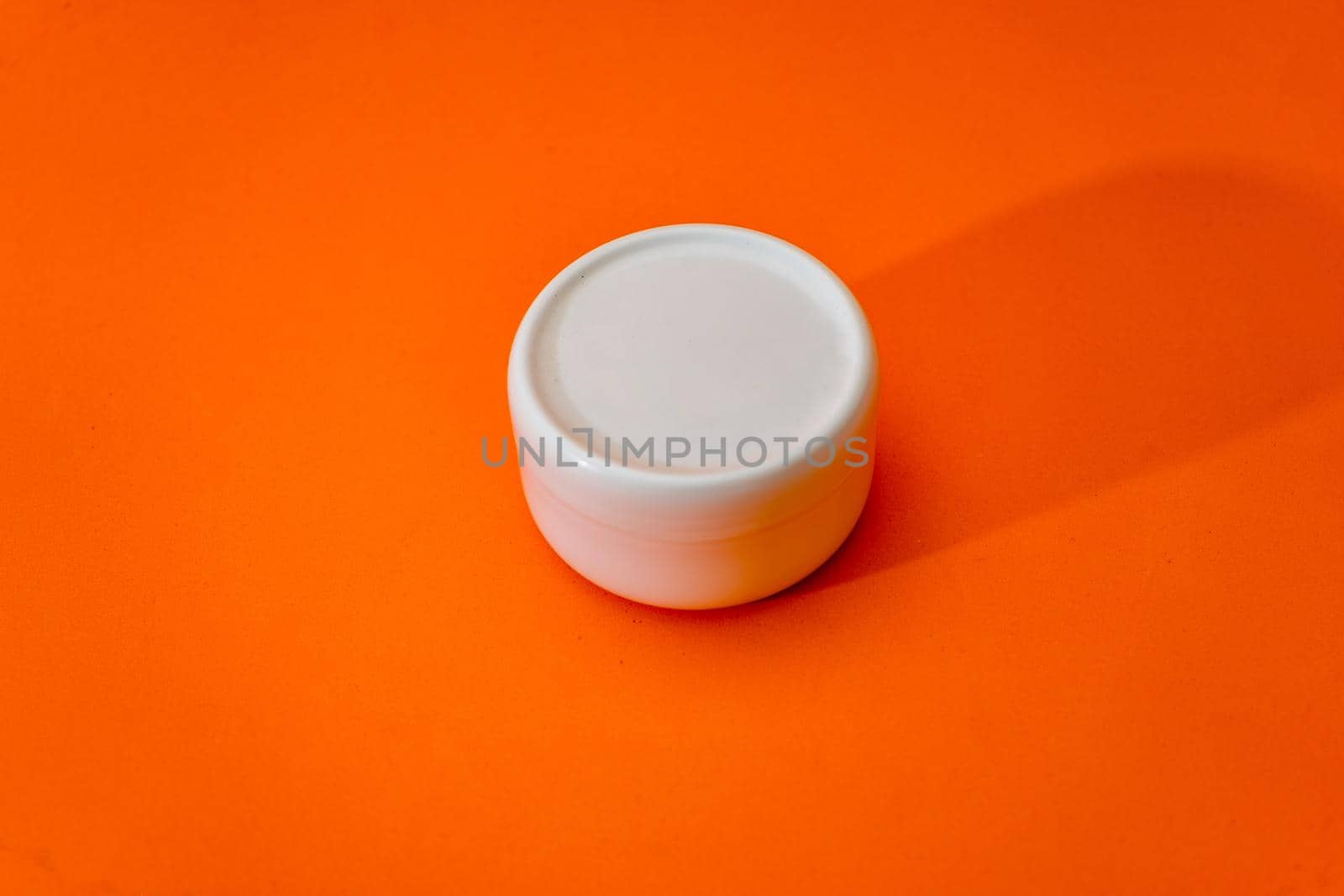 Small white plastic cream jar with lid isolated on orange background. copy space.