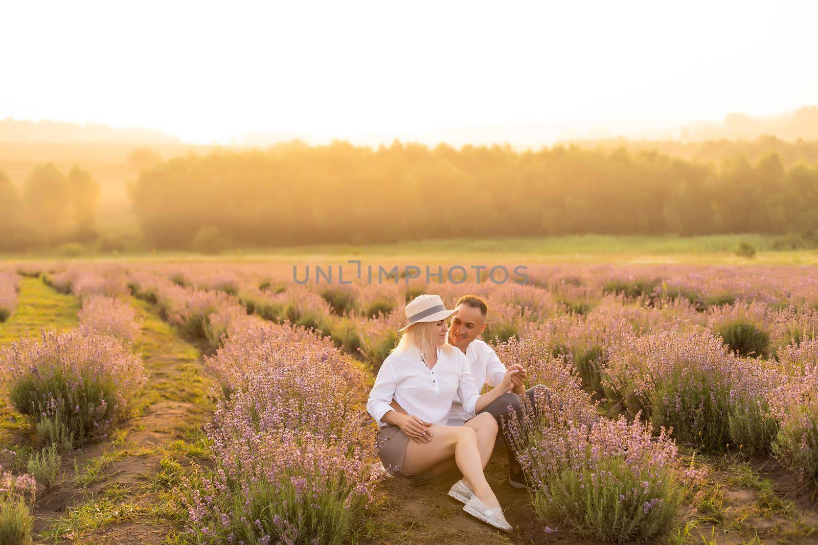 Handsome man with attractive woman lying down on fresh lavender field, enjoying each other, romantic relationship, love concept.