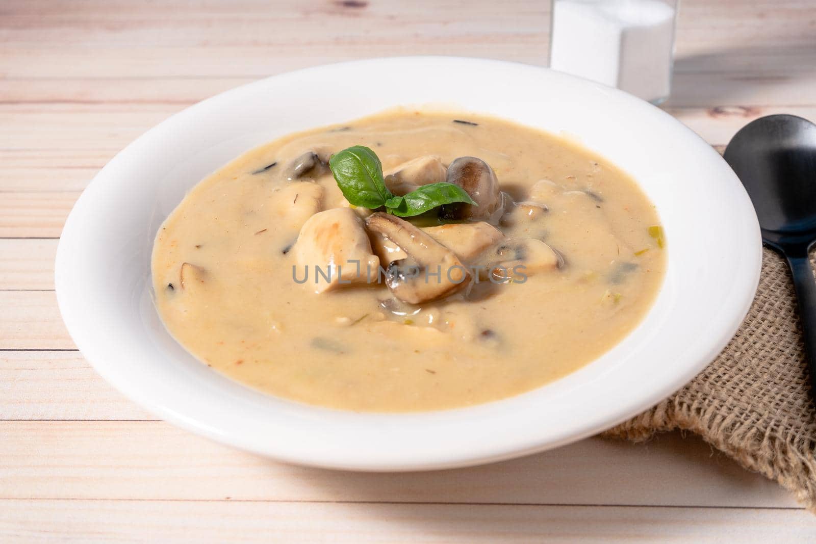 A Homemade cream of chicken and mushroom soup or French style chicken fricassee, in a white soup bowl on a wooden table. High view.