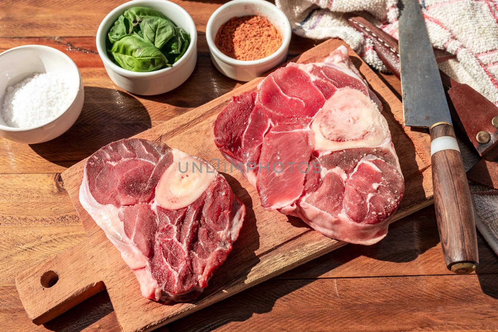 Two steaks of raw beef ossobuco on a wooden board with seasoning to flavour the pieces of meat. Animal protein concept, cheap cuts of beef. Aereal view.