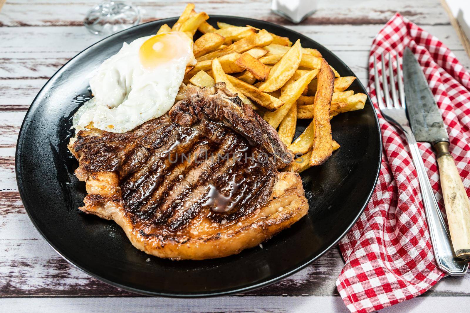 Plate with a juicy t-bone grilled or barbecued, accompanied by a portion of french fries and a fried egg. High view. Traditional, homemade food concept.