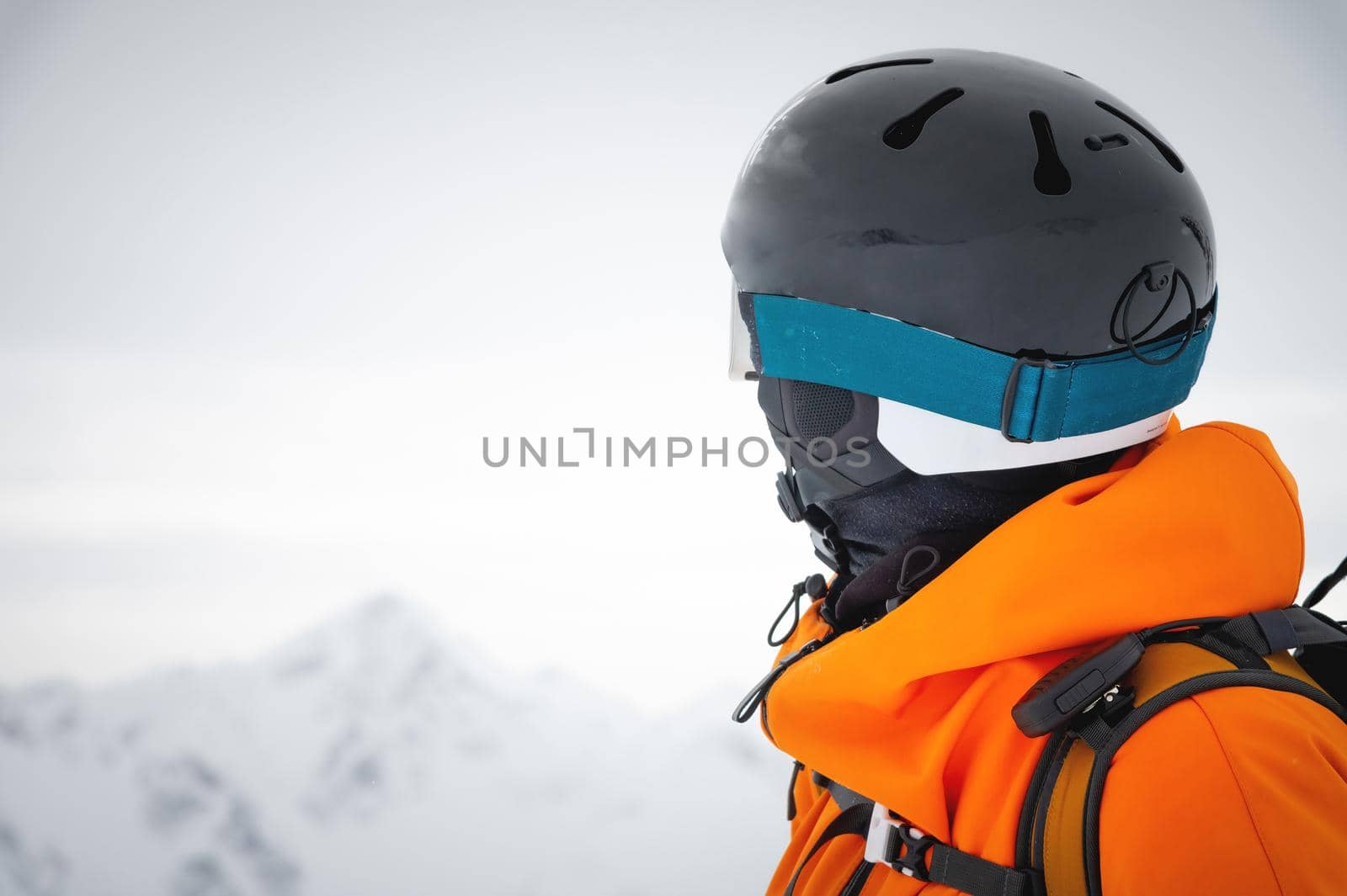 A professional skier athlete in a red jacket, helmet and mask stands on a slope against the backdrop of a glacier and epic mountains. Freeride concept by yanik88