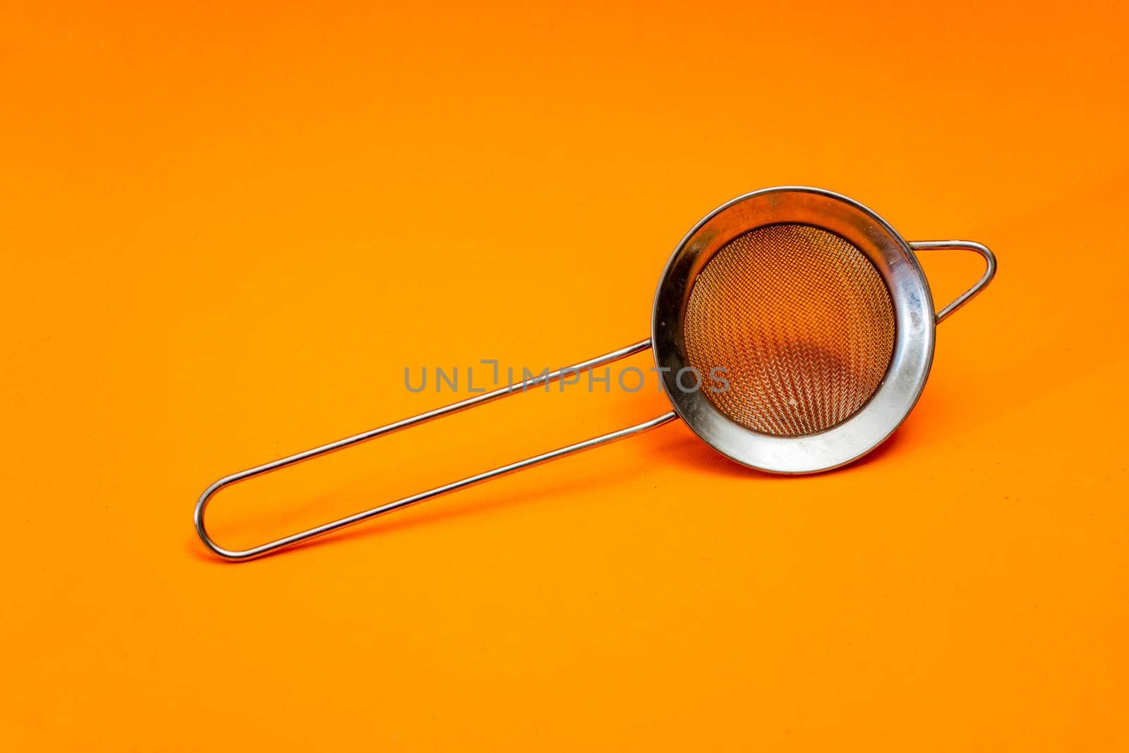 Hand strainer with fine metal mesh insulated on orange bottom.