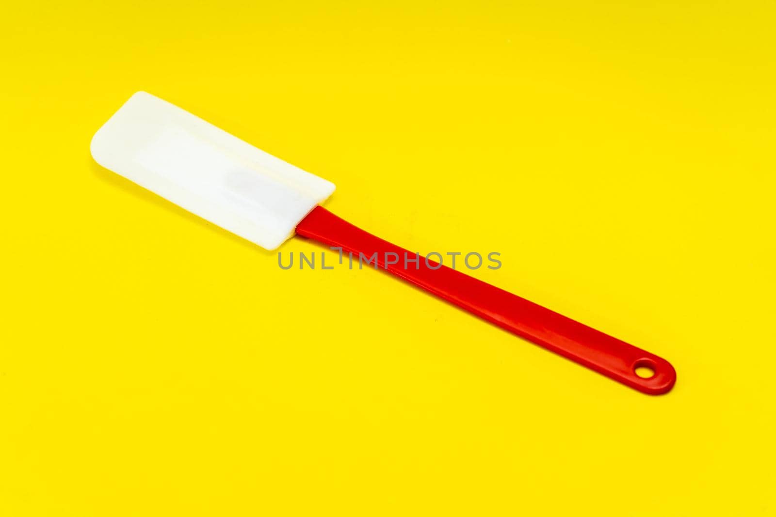 Red and white kitchen spatula made of silicone and plastic insulated on a yellow surface. Kitchen and pastry utensil.